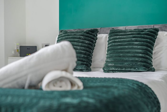 A made-up bedroom with green cushions and fresh towels